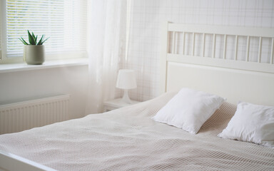 The interior of the room in white tones with a bed, bedside table, table lamp and a flower on the windowsill