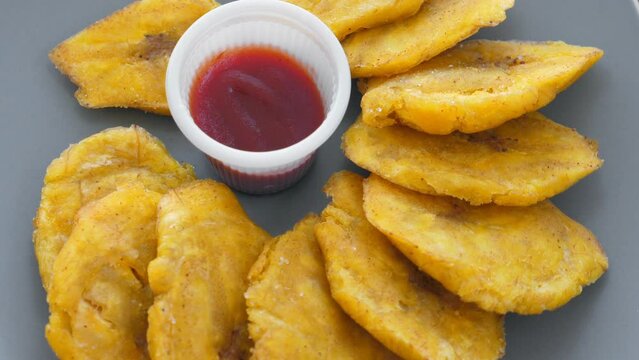 Fried platanos and sauce on plate. Sliced and cooked tostones. Rotating