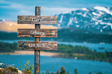 give others grace text quote written on wooden signpost outdoors in nature with lake and mountain...