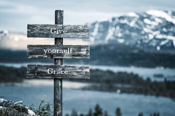 give yourself grace text quote written on wooden signpost outdoors in nature with lake and mountain...