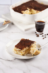 A piece of italian dessert tiramisu made of ladyfinger biscuits, mascarpone cheese, espresso on white marble background