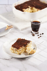 A piece of italian dessert tiramisu made of ladyfinger biscuits, mascarpone cheese, espresso on white marble background
