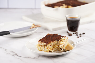 A piece of italian dessert tiramisu made of ladyfinger biscuits, mascarpone cheese, espresso on white marble background