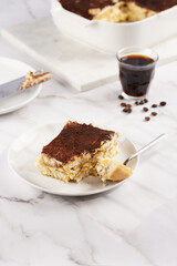A piece of italian dessert tiramisu made of ladyfinger biscuits, mascarpone cheese, espresso on white marble background