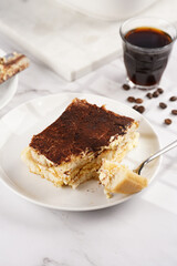 A piece of italian dessert tiramisu made of ladyfinger biscuits, mascarpone cheese, espresso on white marble background