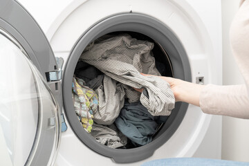 Washing machine with clean laundry. Woman hand pulling out washed bed linen from drum of washing machine. - obrazy, fototapety, plakaty