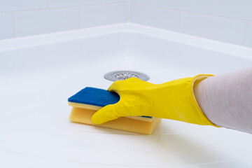 Hand in rubber glove cleaning acrylic shower tray.