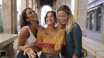 Three happy women using mobile phone outdoors. Group of smiling female friends watching social media at smartphone - Powered by Adobe