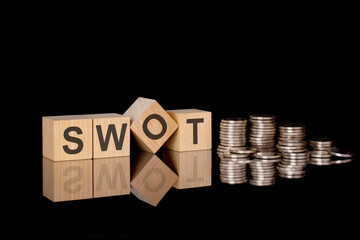 SWOT - text on wooden cubes on dark backround with coins. business concept