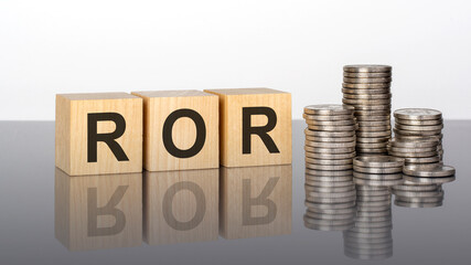 ror - text on wooden cubes on a cold grey light background with stacks coins