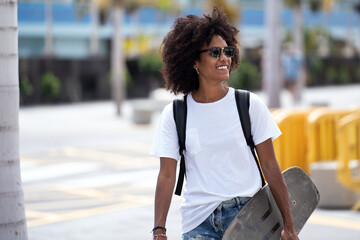 Happy girl with beautiful smile in trendy street style clothes enjoying riding skateboard at sunny day. Real people lifestyle.