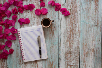 Libreta rayada, flores, café y pluma en una mesa desgastada de madera