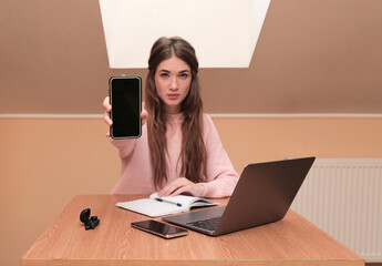 young beautiful girl working at a laptop shows the phone into the camera. workplace. business. success