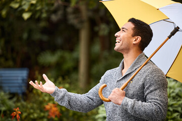 When it rains, it pours. Shot of a young man standing in the rain with an umbrella.