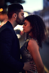 Fototapeta premium Special loving moments. Shot of a cheerful young couple holding one another while sharing a kiss on the forehead outside at night.