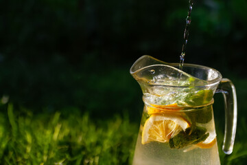 Defocus water drops and bubbles splashing pouring in glass jug of lemonade with slice lemon and...