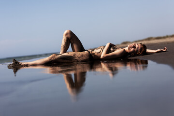 Sexy female body covered with sand. Girl on a beach with sea water reflection. .