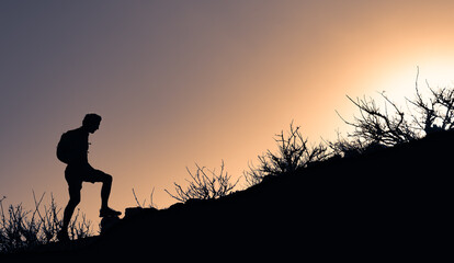 Hiker silhouette starting his climb up the mountain. Outdoor adventure, motivation and active sport concept.	