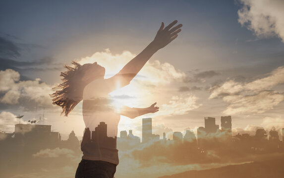 Faith hope and freedom concept. Woman with arms raised to the sunrise city sky. 