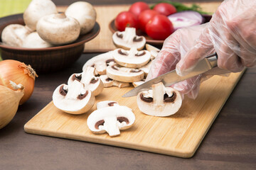 Chef cutting, slicing mushrooms champignon close up. Hands in gloves cooking healthy vegetables vegetarian vegan diet food
