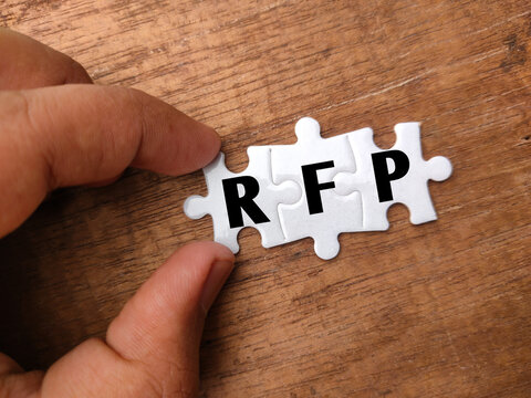 Hand holding white puzzle with word RFP on wooden background.