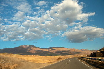 Landscape with a road among autumn yellow mountains at sunny day with low white clouds