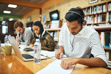 Hes focused on his studies. Cropped shot of a young male university student studying in the library with other students in the background.