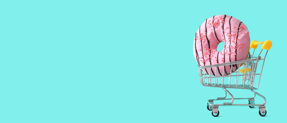 Shopping cart with sweet tasty donut on color background with space for text © Pixel-Shot
