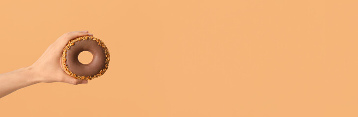 Hand holding tasty donut on color background with space for text