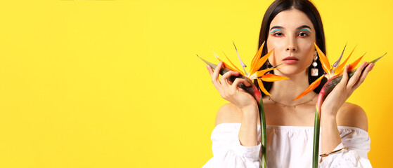 Pretty young woman holding strelitzia flowers on yellow background with space for text