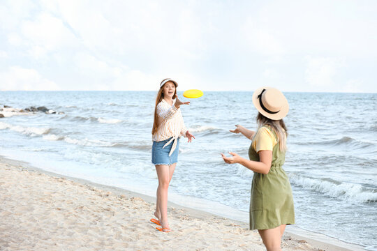 Happy young women playing frisbee on sea beach