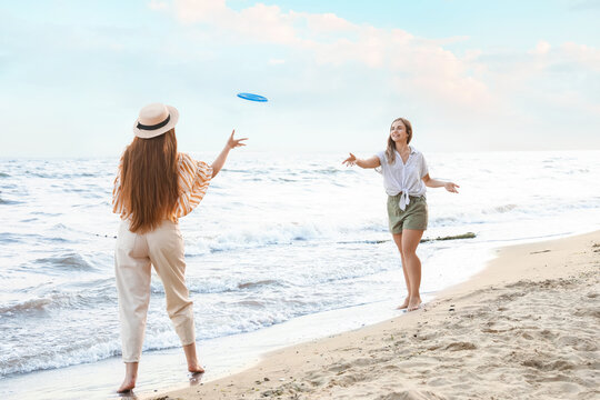 Happy young women playing frisbee on sea beach
