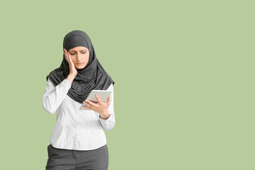 Sad Muslim secretary with tablet on color background