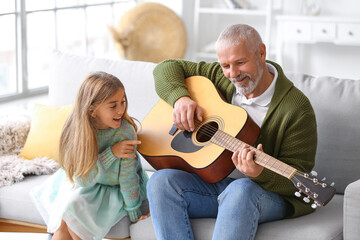 Senior man with his little granddaughter playing guitar at home
