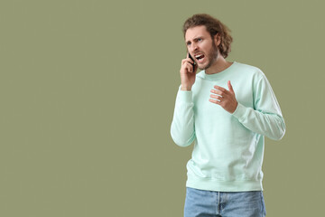 Angry young man talking by mobile phone on green background