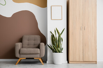 Armchair, houseplant and cabinet near color wall - obrazy, fototapety, plakaty