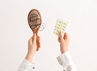 Woman holding brush with fallen down brunette hair and pills on white background