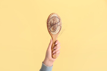 Woman holding brush with fallen down brunette hair on yellow background