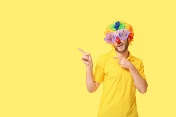 Fototapeta premium Funny young man in disguise showing something on yellow background. April fools' day celebration