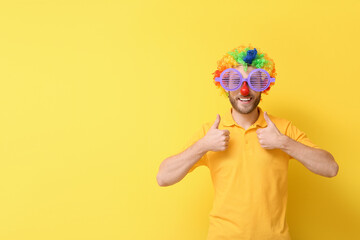 Funny young man in disguise showing thumb-up gesture on yellow background. April fools' day celebration