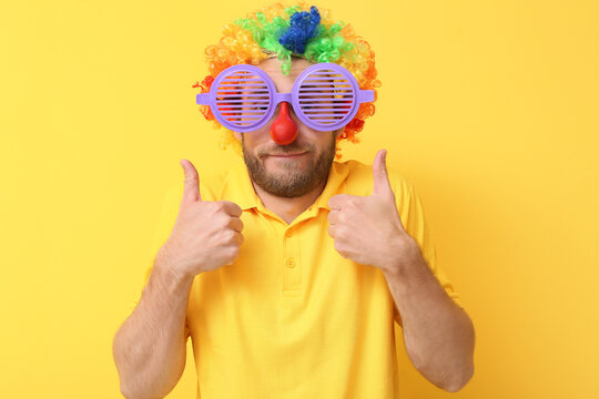 Funny young man in disguise showing thumb-up gesture on yellow background. April fools' day celebration
