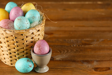 Wicker basket and cup with painted Easter eggs on wooden background