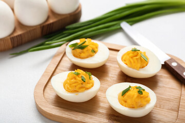 Board with tasty stuffed eggs and knife on white background, closeup. Easter celebration