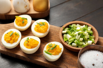 Board with stuffed eggs, salt and green onion on dark wooden background. Easter celebration