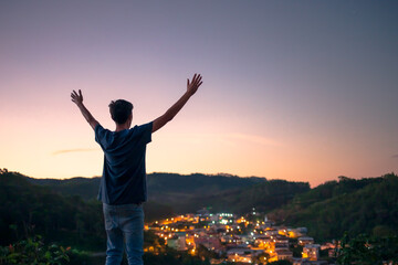 Fototapeta na wymiar Man with arms raised thanking and worshiping God, under the dusk sky and with city lights in the background. Concept of faith, religion or spirituality.