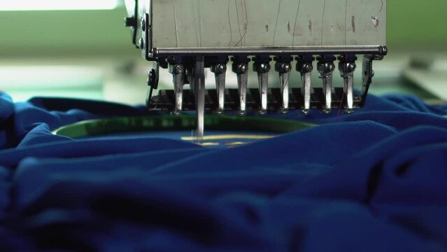 Close-up automatic embroidery machine is working at high speed. Embroidery machine embroidering logo on a T shirt.