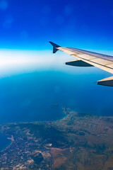 View from the airplane window at a beautiful blue clear sky, earth, sea and the airplane wing