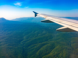 View of airplane wing, blue skies and green land during landing. Airplane window view.