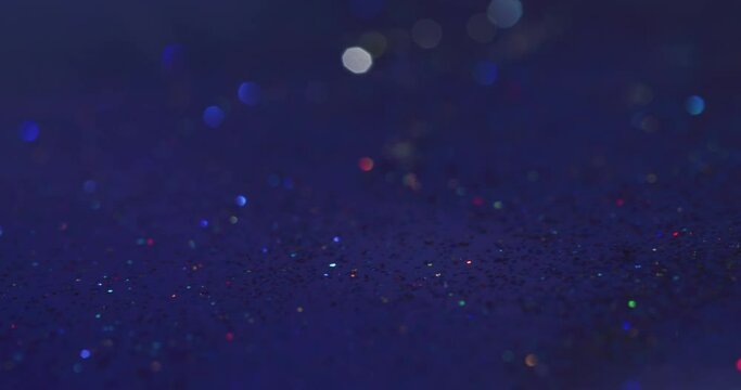 Glitter abstract background. Bokeh light. Glitz gleam. Defocused neon colorful sparkling circles falling motion on dark blue grain texture overlay shot on RED Cinema camera.