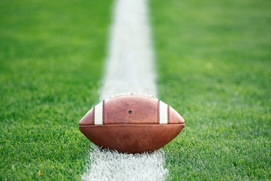 Close up view of an American Football sitting on a grass football field on the yard line. Generic Sports image